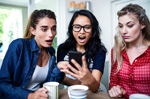 Young female friends shocked while looking in mobile phone at home