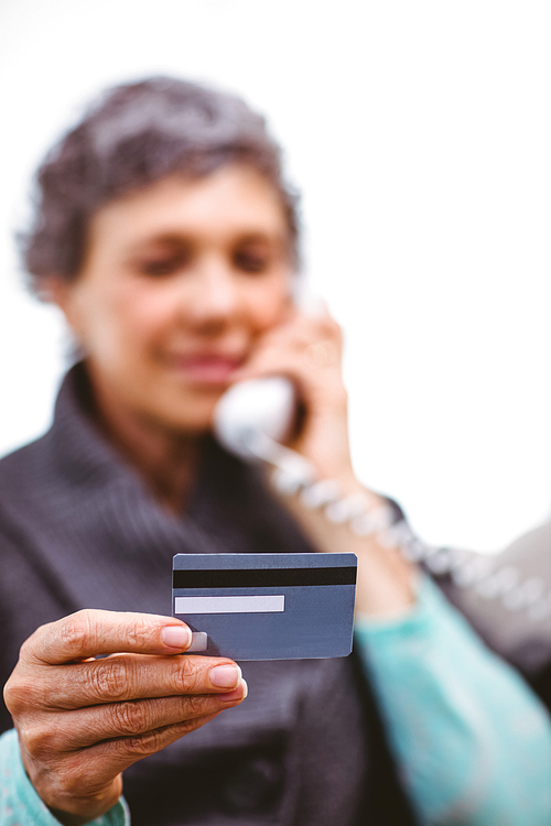 Close-up of mature woman holding payment card while talking on telephone at home