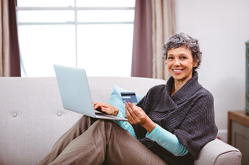 Portrait of happy mature woman with credit card using laptop at home