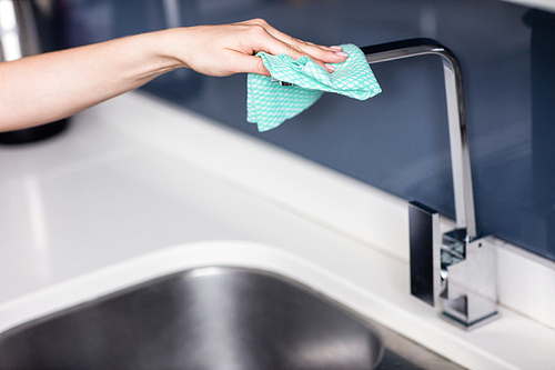 Cropped hand of woman wiping faucet by sink in kitchen