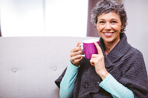 Portrait of happy mature woman with coffee mug sitting on sofa at home