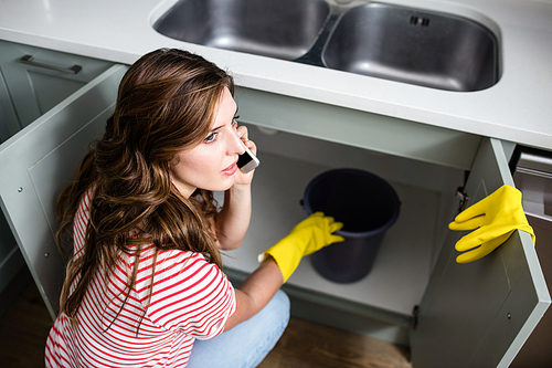 Woman talking on mobile phone while holding bucket at kitchen sink