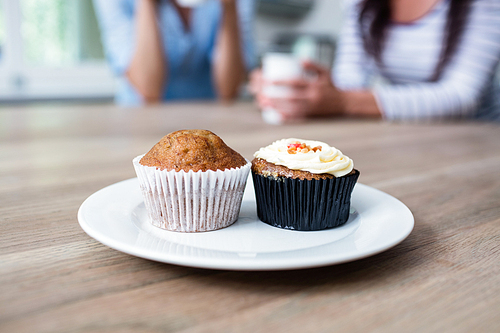 Muffin and cupcake served in plate on table with friends sitting in background at home