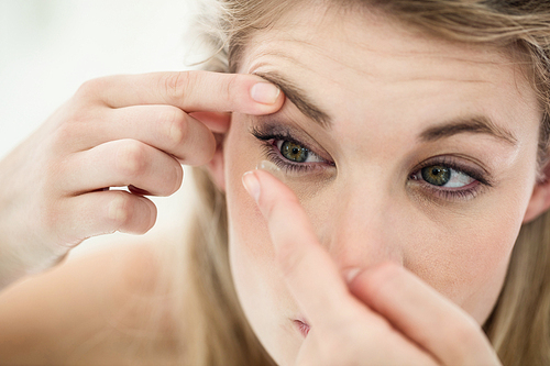 Close-up of young woman applying contact lens while in bathroom