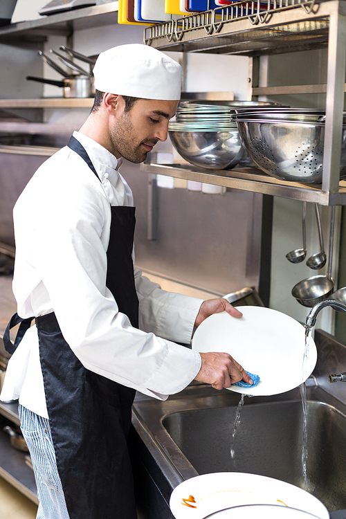 Handsome employee doing dishes in commercial kitchen