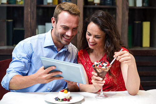 Happy couple using digital tablet while having desert at restaurant