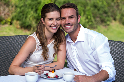 Portrait of smiling happy couple sitting on chair in park