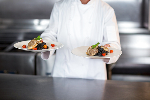 Midsection of chef holding plates while standing in commercial kitchen