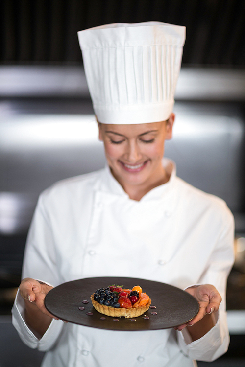 Happy female chef holding plate of dessert in commercial kitchen