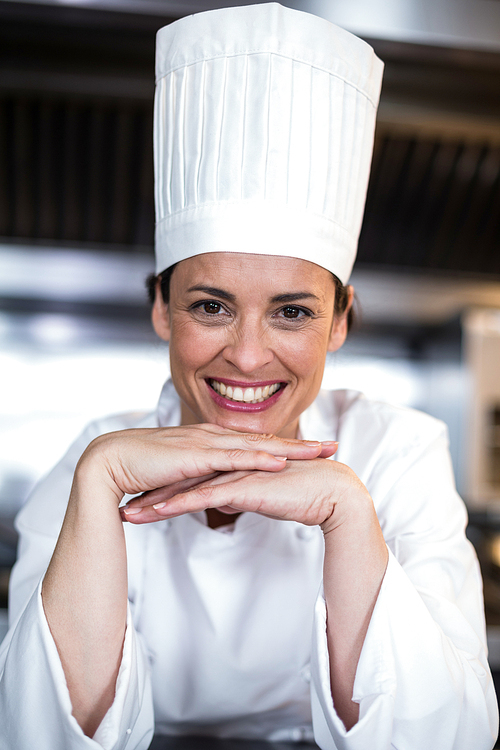 Portrait of happy female chef with hands on chin in commercial kitchen