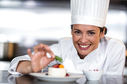 Portrait of happy female chef garnishing on food in commercial kitchen