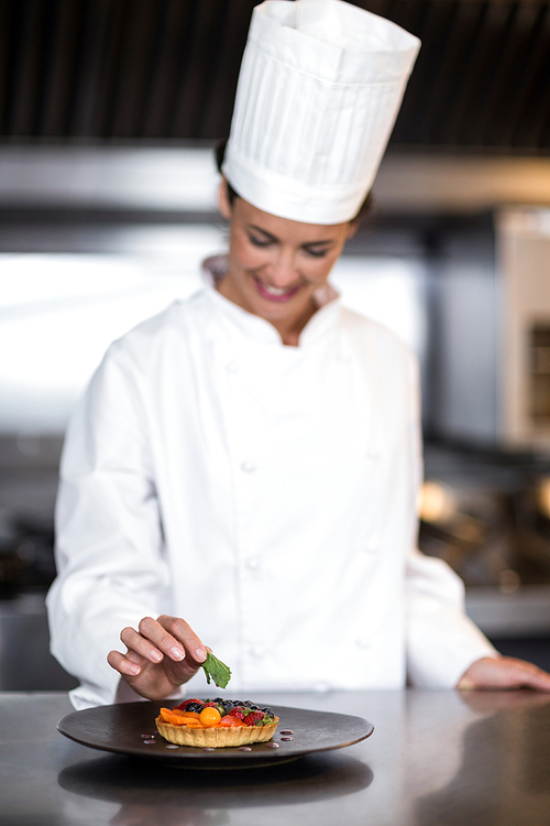 Happy female chef garnishing on food while standing in commercial kitchen