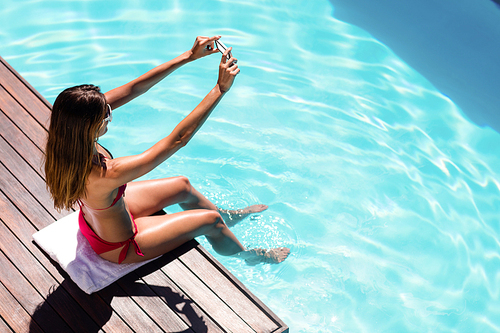 Woman taking a selfie on the pool edge on a sunny day