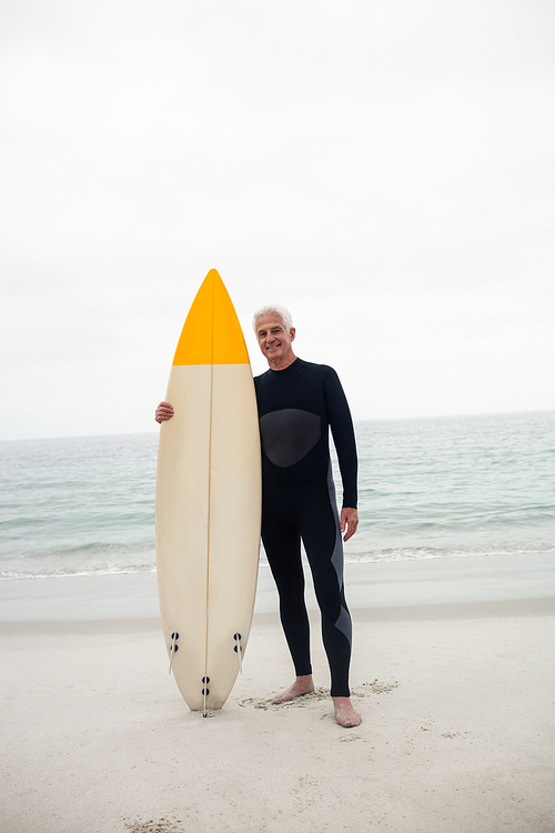 Portrait of senior man in wetsuit holding a surfboard on the beach