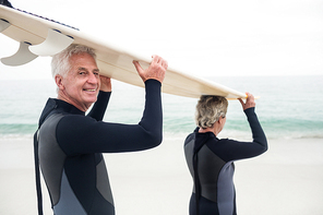 Senior couple in wetsuit carrying surfboard over head on the beach