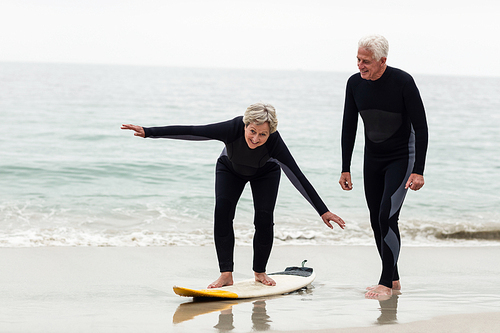 Senior man teaching woman to surf on beach