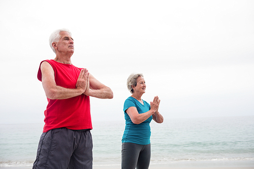 Senior couple in lotus position on the beach on a sunny day