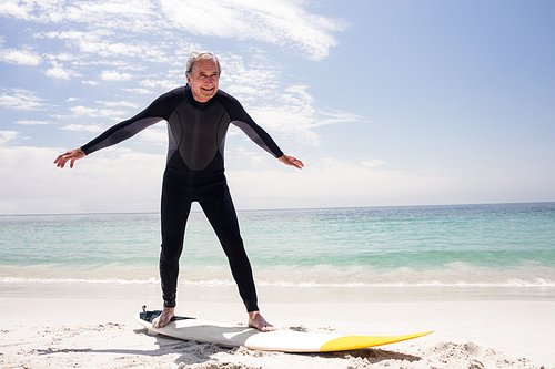 Happy senior man in wetsuit standing on surfboard at beach