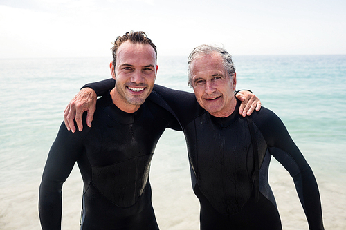 Portrait of happy father and son in wetsuit embracing on the beach on a sunny day