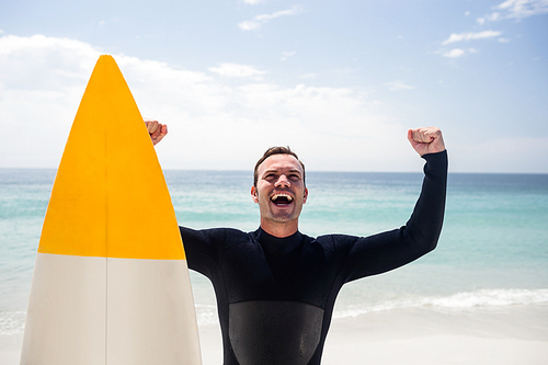 Happy man with surfboard standing on the beach with arms outstretched