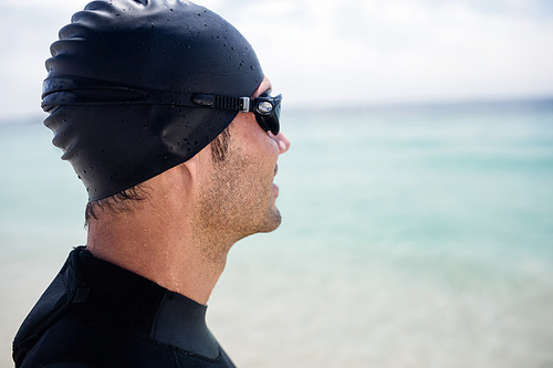 Young man in wetsuit and swimming goggles standing on beach on a sunny day