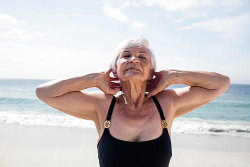 Senior woman performing neck exercise on beach