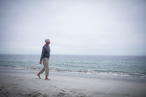 Thoughtful retired man walking on the beach on holidays