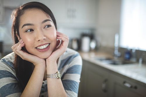 Happy young woman daydreaming in kitchen at home
