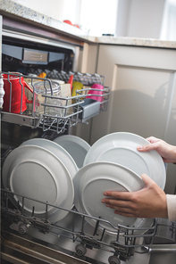 Woman in kitchen arranging plates in dish washer