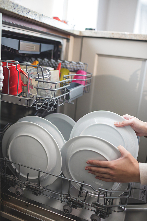 Woman in kitchen arranging plates in dish washer