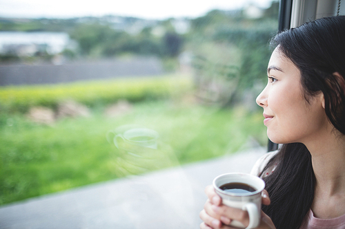 Happy woman holding a coffee cup and looking through window