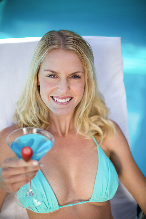 Beautiful woman in bikini holding a martini glass while relaxing on sun lounger near pool