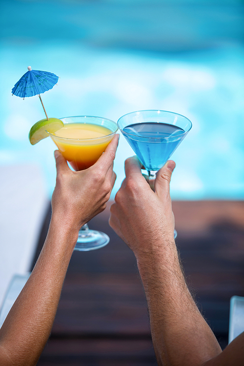 Hands of couple toasting martini glass near pool