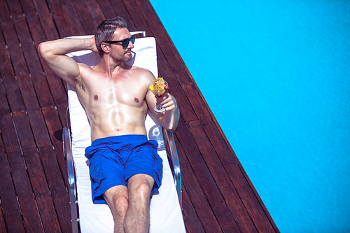 Man holding a martini glass while relaxing on a sun lounger near the pool