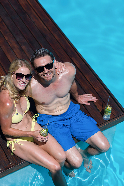 Couple in sunglasses sitting at poolside side with glass of mojito