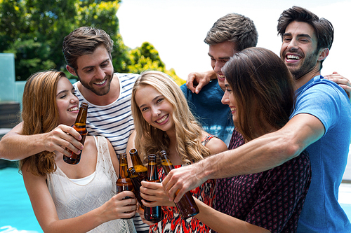 Group of friends toasting beer bottles while enjoying near pool