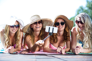 Group of friends taking selfie with selfie stick near pool