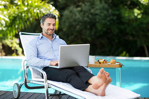Smart man relaxing on sun lounger and using a laptop near the pool