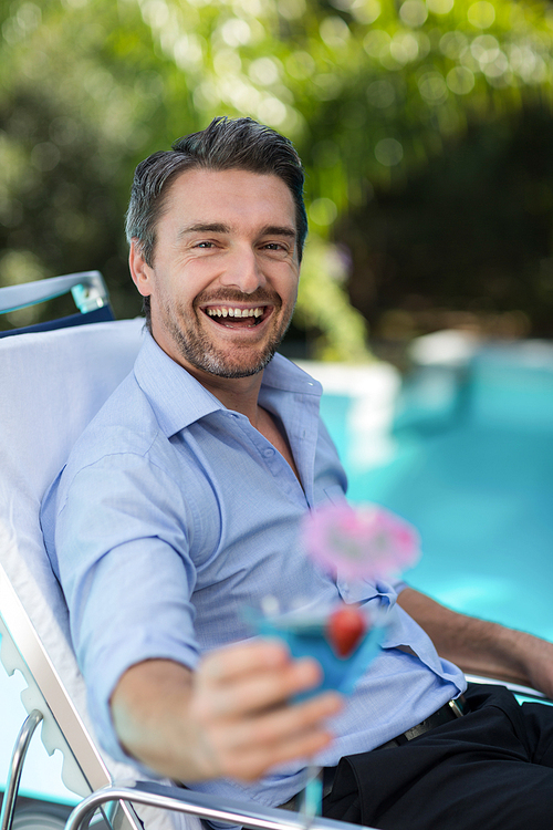Smart man holding martini glass while relaxing in sun lounger near pool