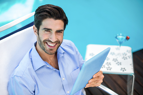 Portrait of smart man relaxing on sun lounger and using a digital tablet near pool