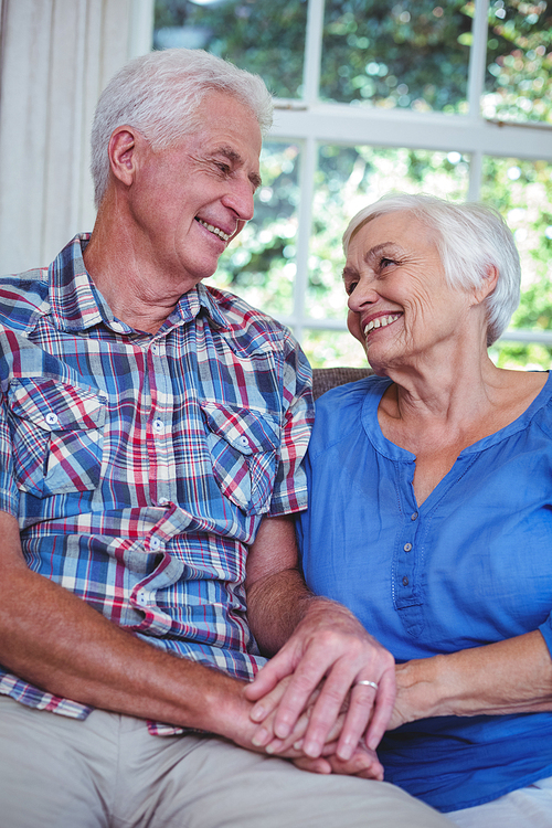 Smiling senior couple holding hands while sitting on sofa at home