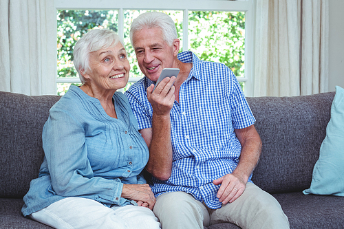 Cheerful senior couple listening to music through phone at home