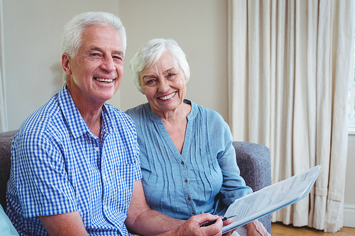 Portrait of happy senior couple with bills while sitting on sofa at home