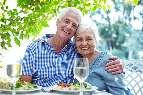 Portrait of happy retired couple with arm around while sitting at table