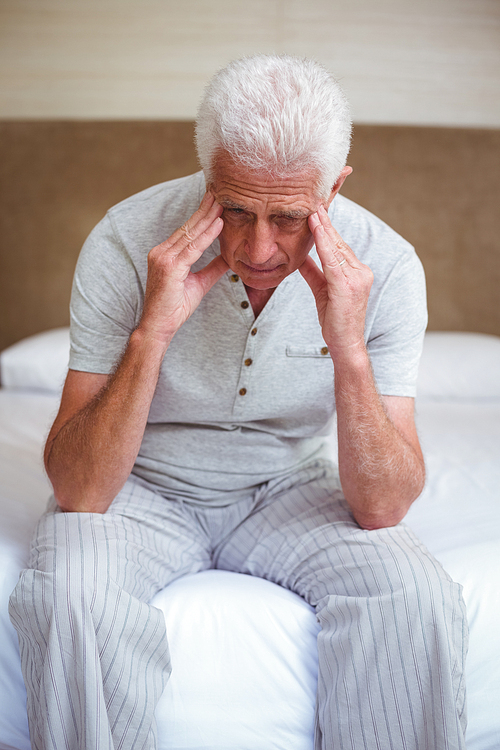 Tensed senior man with head in hands while sitting on bed