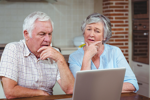 Thoughtful senior couple using laptop at home