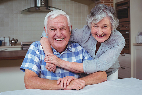 Portrait of happy senior woman embracing man from behind in kitchen