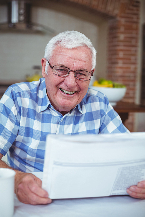 Happy senior man with newspaper in kitchen