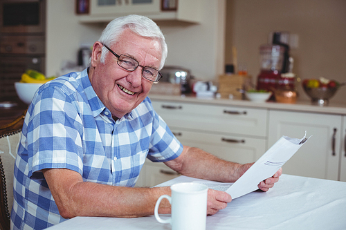 Portrait of senior man with newspaper in kitchen