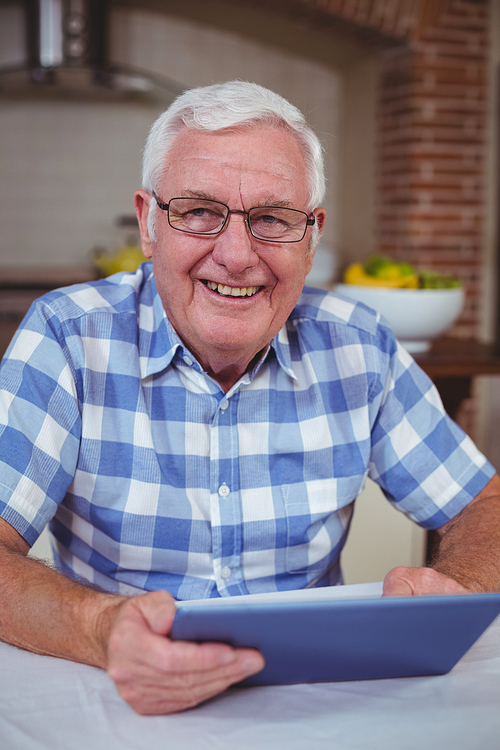 Portrait of senior man with digital tablet while sitting in kitchen
